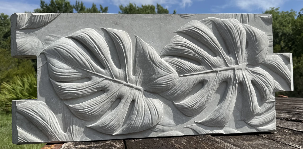 Close view of the sculpted monstera-leaf relief on a concrete garden-bed panel