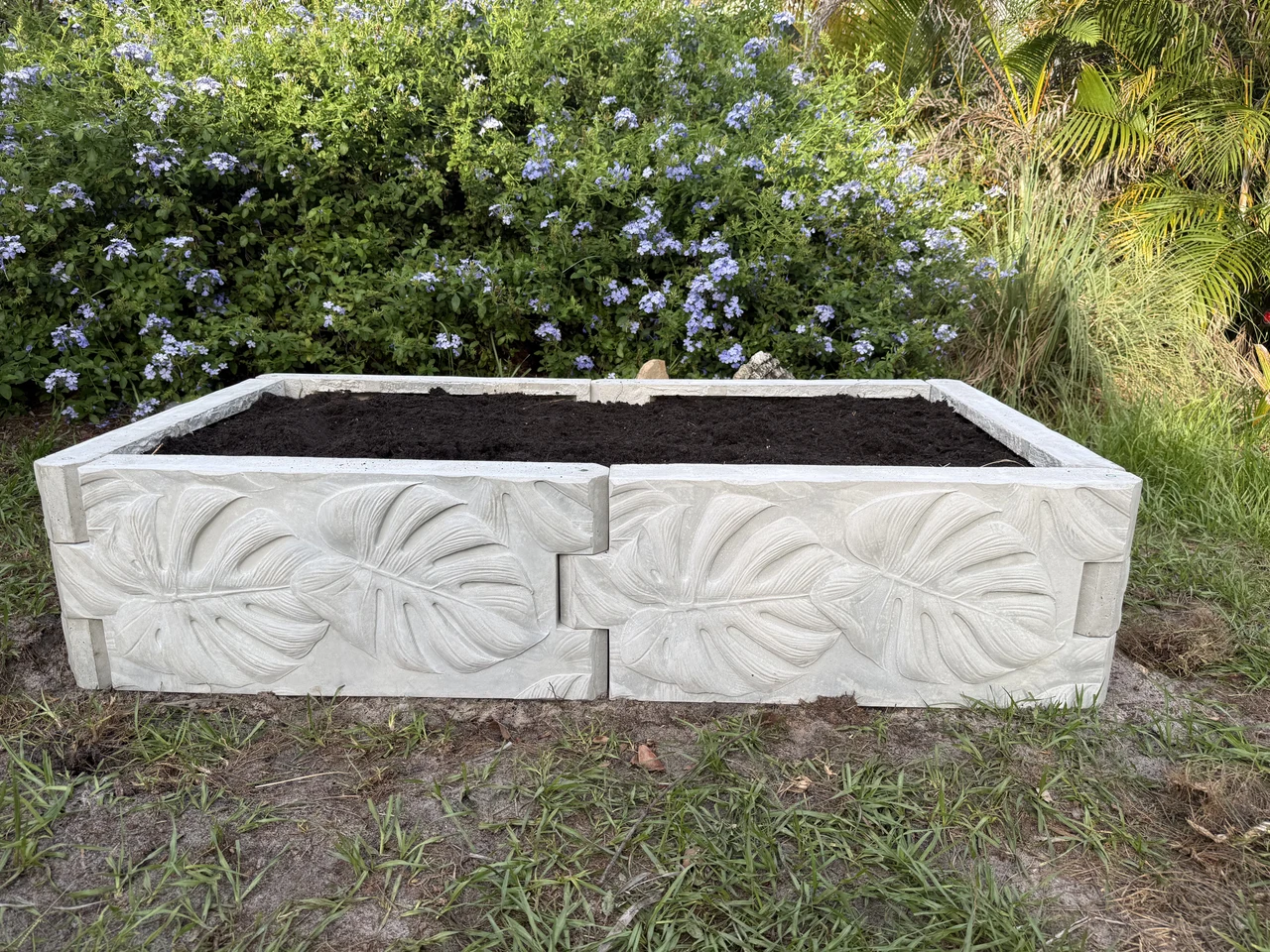 Straight-on view of a completed rectangular concrete garden bed assembled from botanical-relief panels