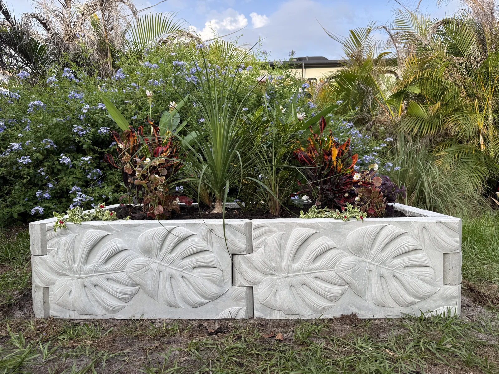 A planted concrete raised bed assembled from sculpted leaf-pattern panels